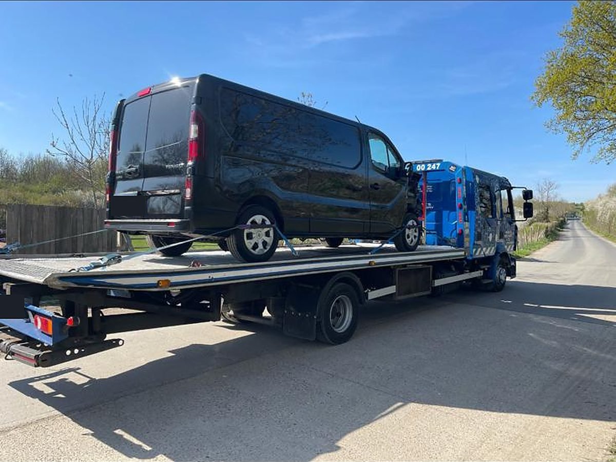 Black van strapped down on a flatbed recovery truck