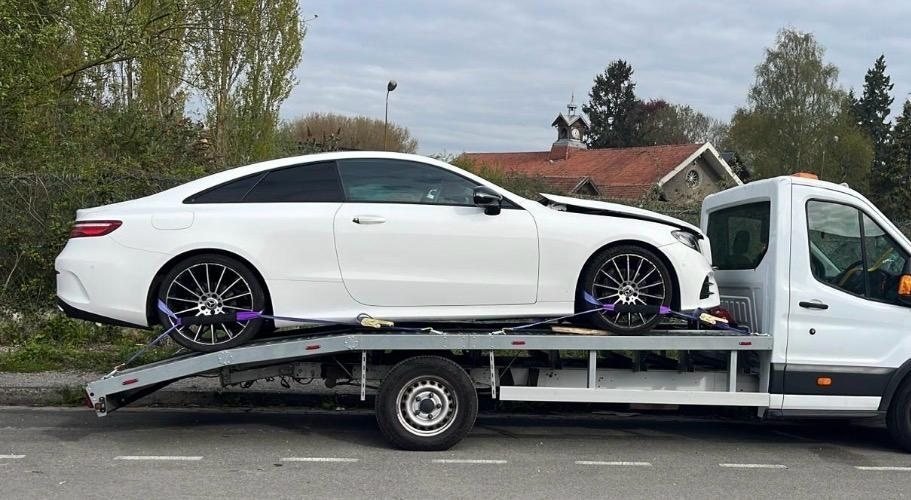 White coupe strapped down on a flatbed recovery truck