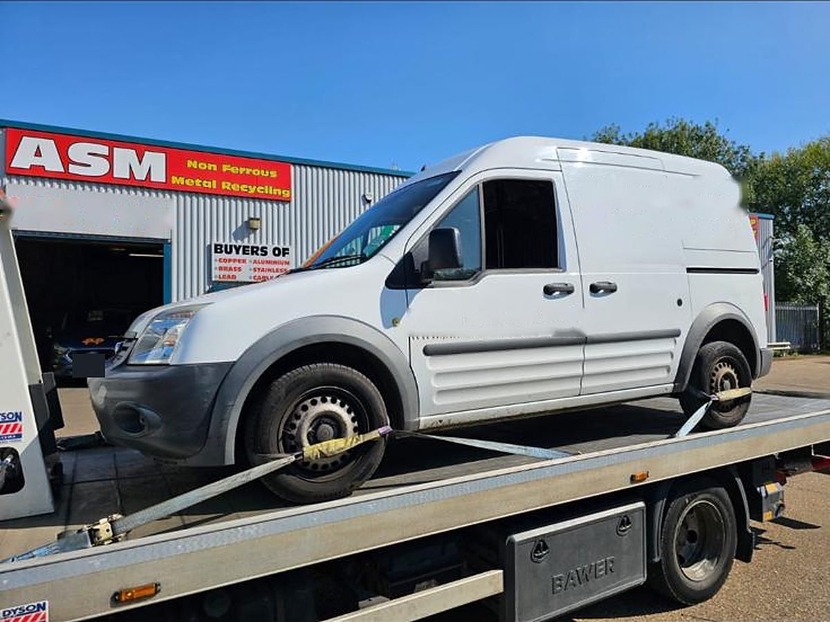 White Ford Transit Connect van strapped onto a flatbed recovery truck