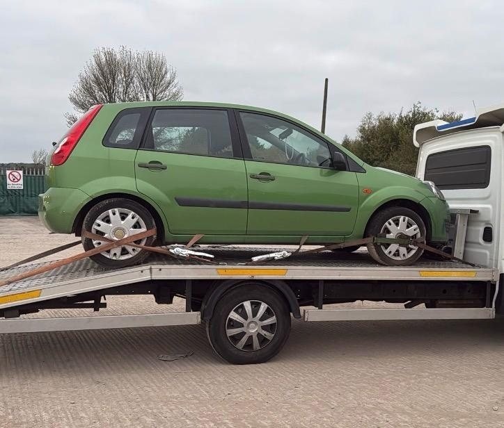 Green hatchback strapped down on a flatbed recovery truck