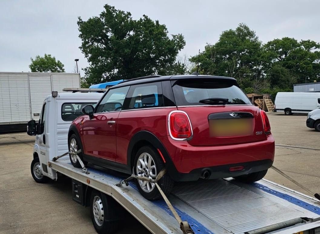 Red Mini hatchback strapped down on a flatbed recovery truck