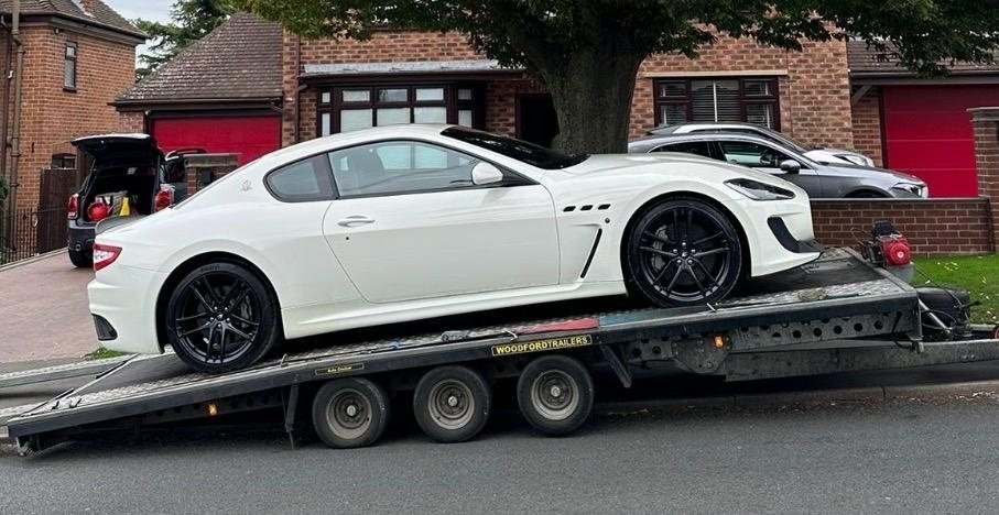 White Maserati sports coupe loaded on a flatbed recovery trailer
